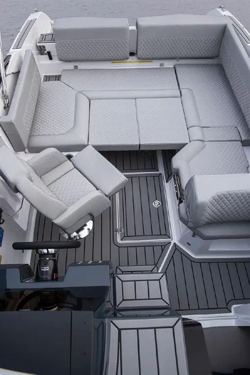 Modern boat interior featuring grey cushioned seating and a steering console on a wooden deck.